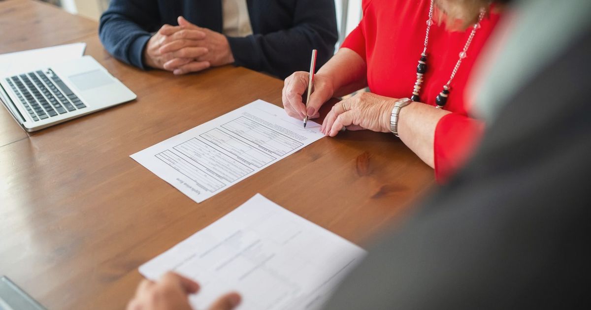 Two adults sign documents on a wooden table at a business meeting, emphasizing teamwork.