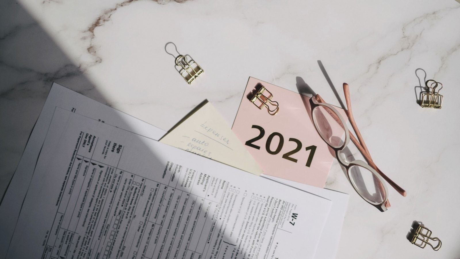 Close-up of tax documents, glasses, and a note labeled 2021 on a marble desk.