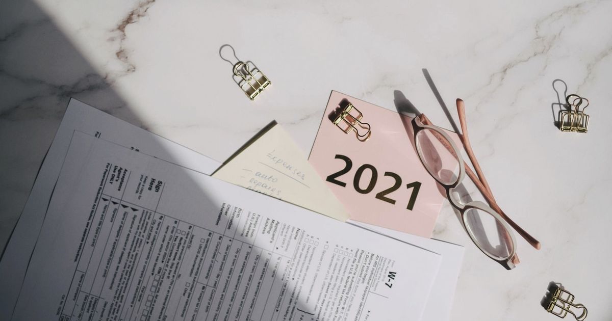 Close-up of tax documents, glasses, and a note labeled 2021 on a marble desk.