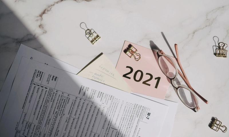 Close-up of tax documents, glasses, and a note labeled 2021 on a marble desk.