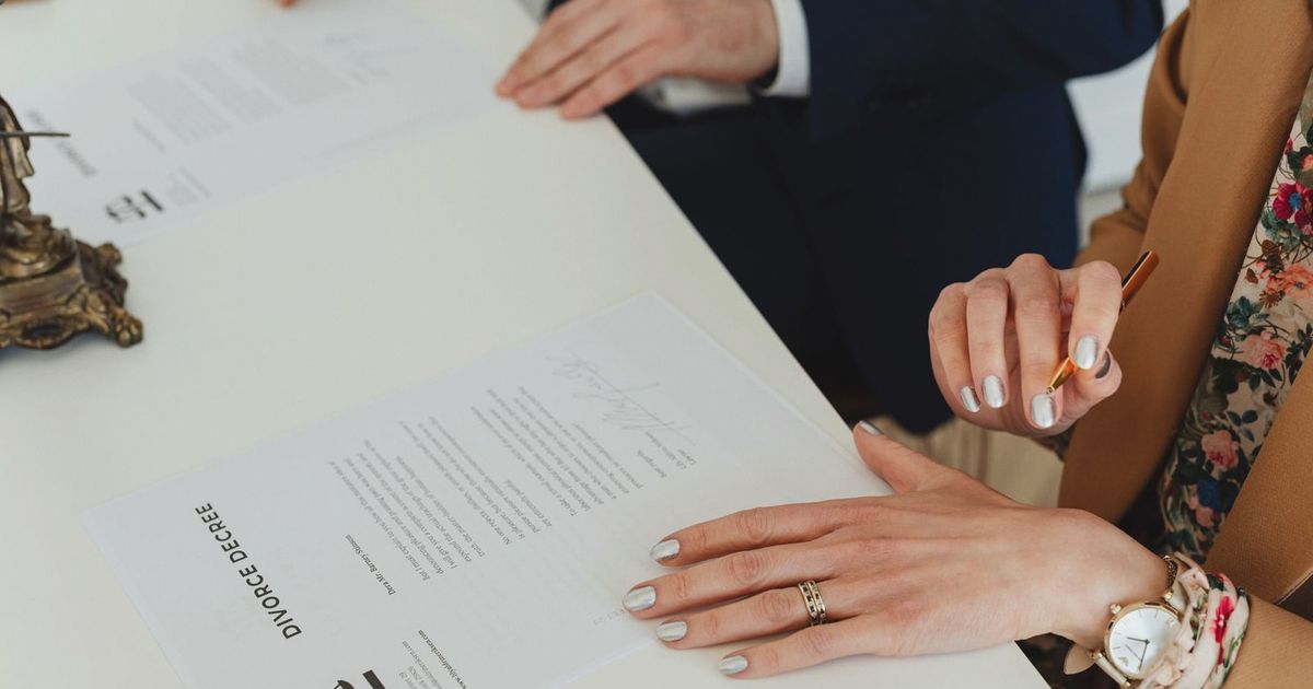 A detailed view of hands signing a divorce decree document at an indoor office meeting.