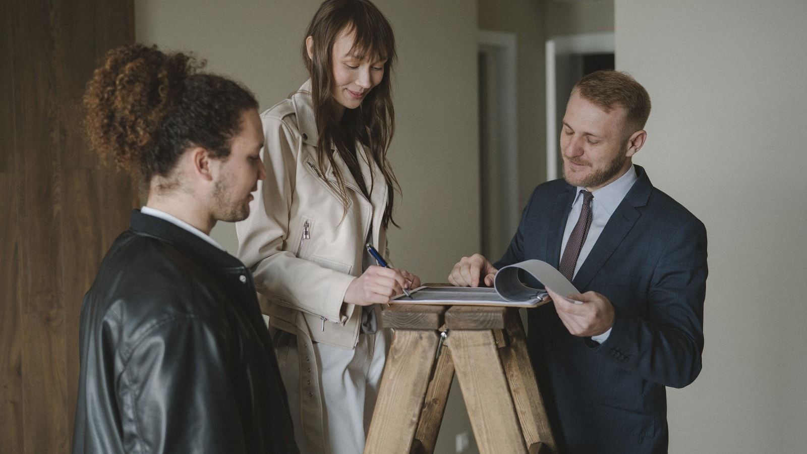 A couple signing real estate documents with a realtor inside a new apartment.