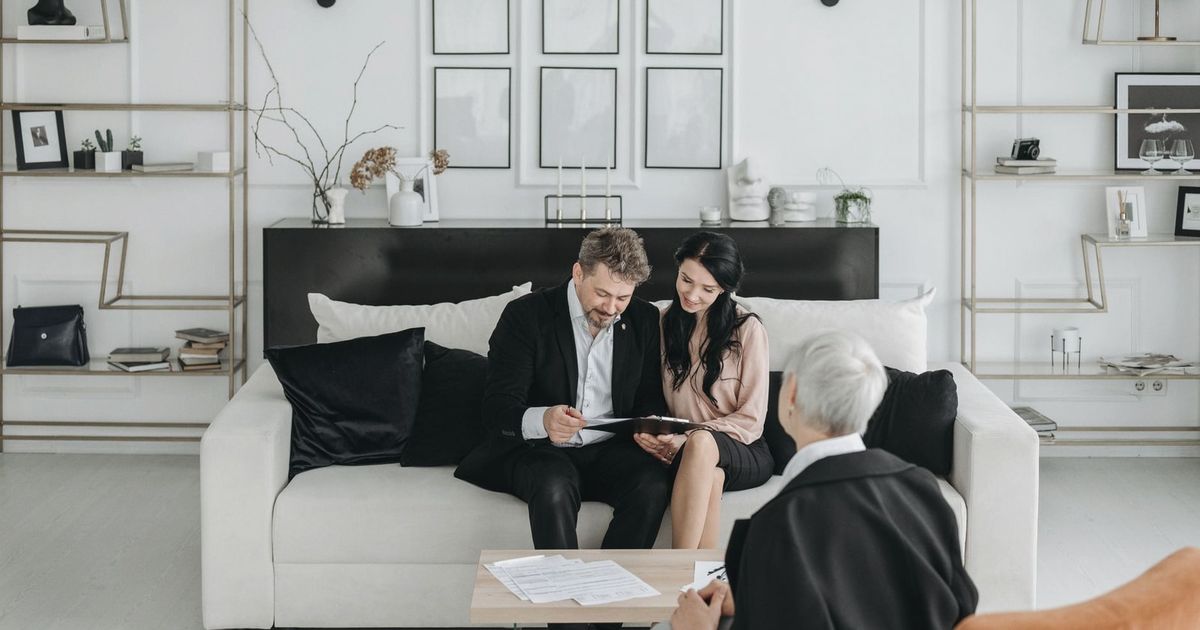 Couple consulting with a social worker in a modern living room setting, discussing documents.