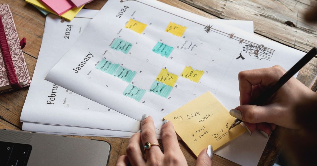 Close-up of a person writing new year's goals on a sticky note with a 2024 calendar in the background.