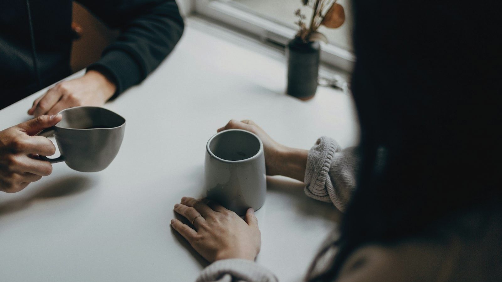 two people holding gray mugs at table
