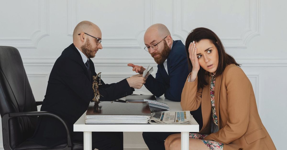 Two lawyers discuss documents with a worried client in a professional office setting.