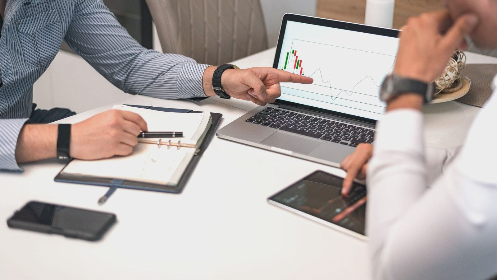 Two businessmen analyzing financial charts and data on a laptop and tablet.