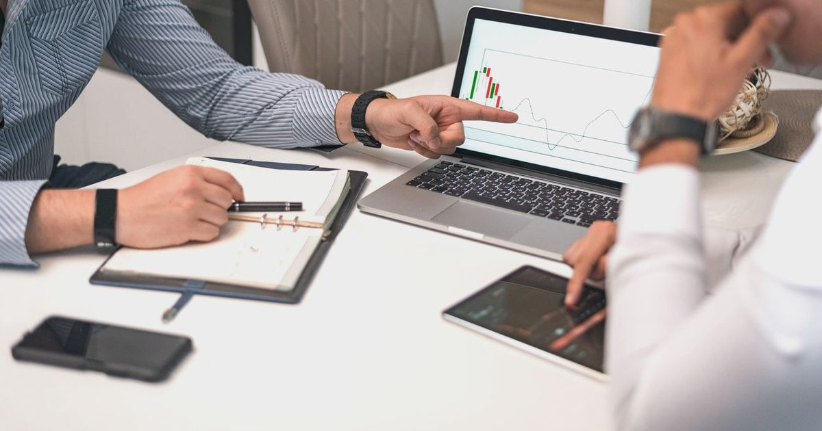 Two businessmen analyzing financial charts and data on a laptop and tablet.