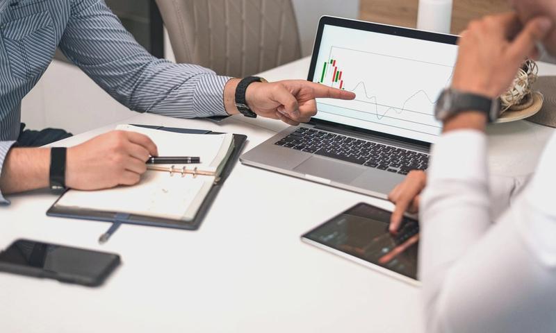 Two businessmen analyzing financial charts and data on a laptop and tablet.