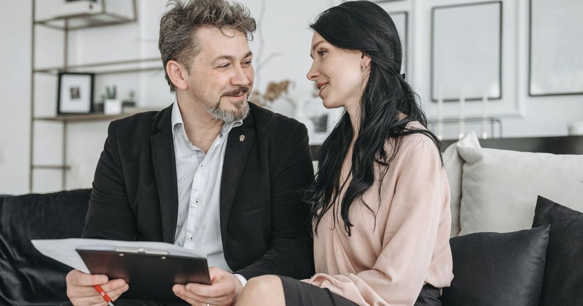 A couple sitting on a couch, smiling, and reviewing documents indoors.