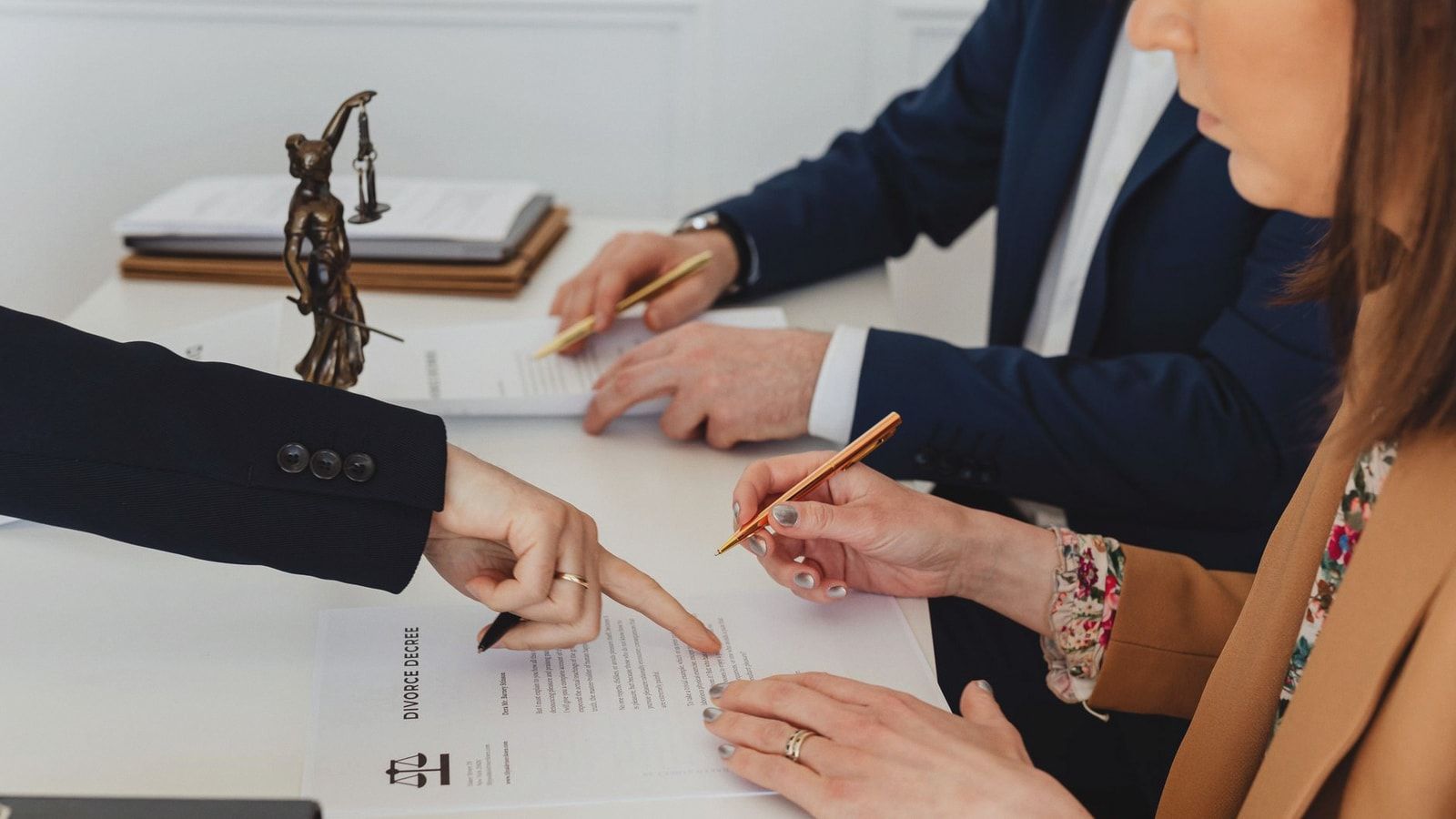 Hands signing a divorce decree, with a justice statue nearby, symbolizing legal proceedings.
