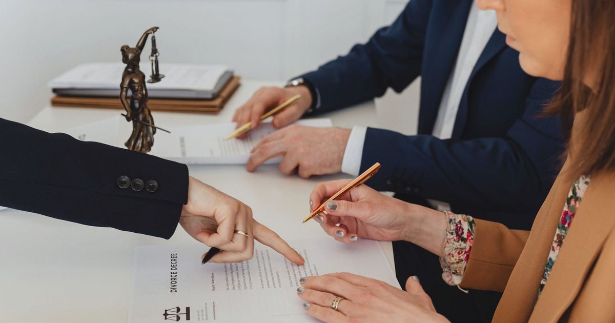 Hands signing a divorce decree, with a justice statue nearby, symbolizing legal proceedings.