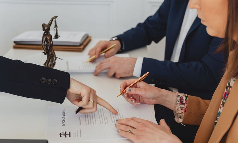 Hands signing a divorce decree, with a justice statue nearby, symbolizing legal proceedings.