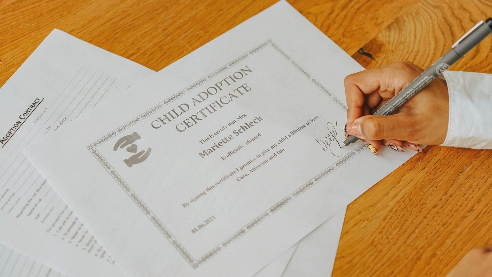 Close-up view of a hand signing an official child adoption certificate document.