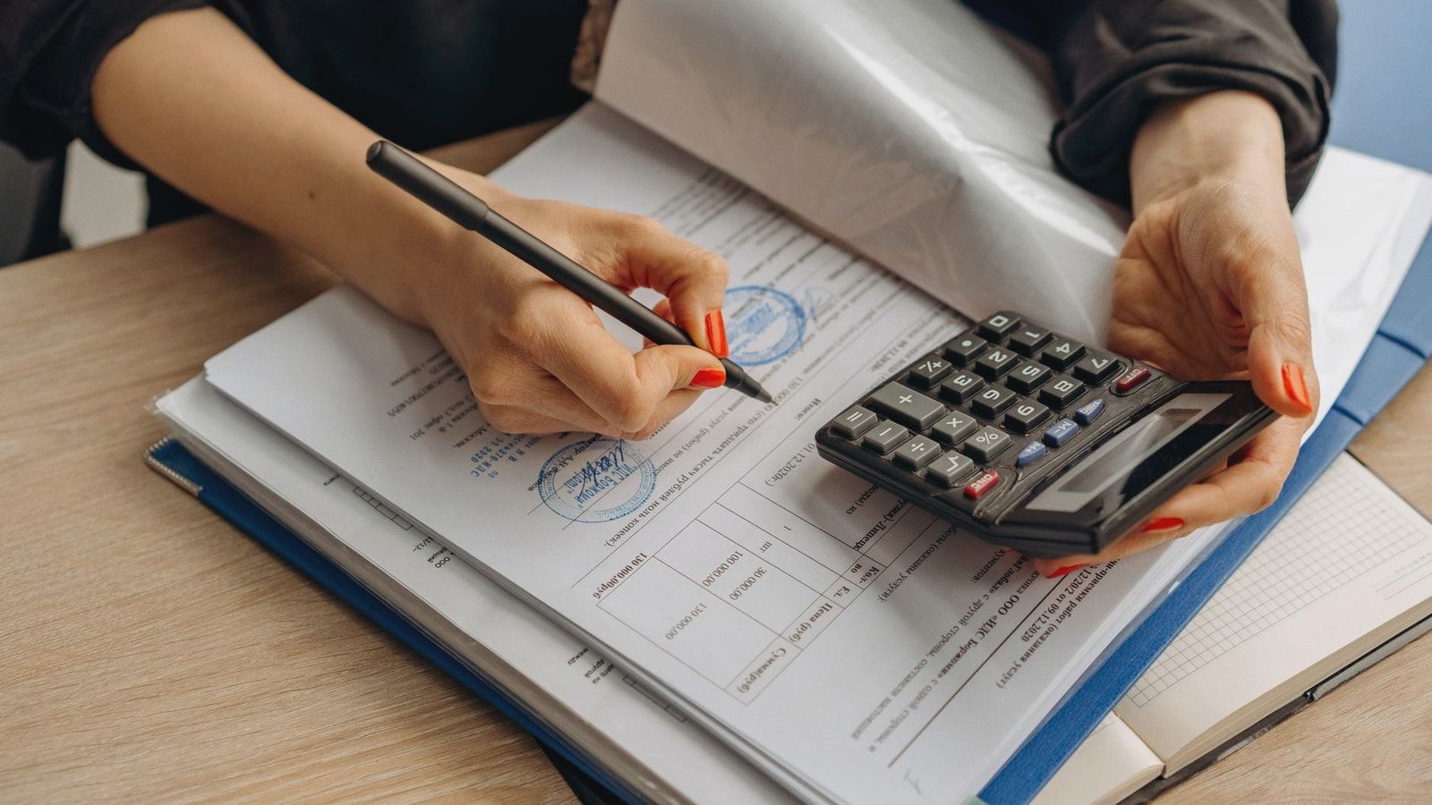 An accountant using a calculator and signing paperwork, showcasing financial analysis.