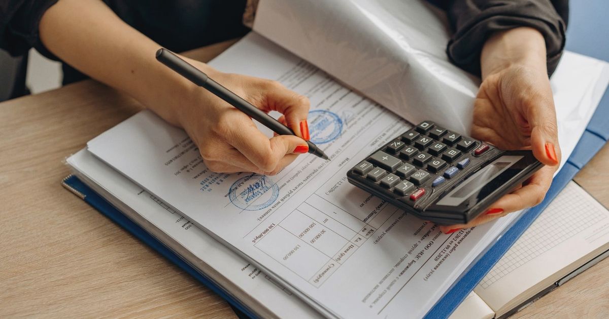 An accountant using a calculator and signing paperwork, showcasing financial analysis.