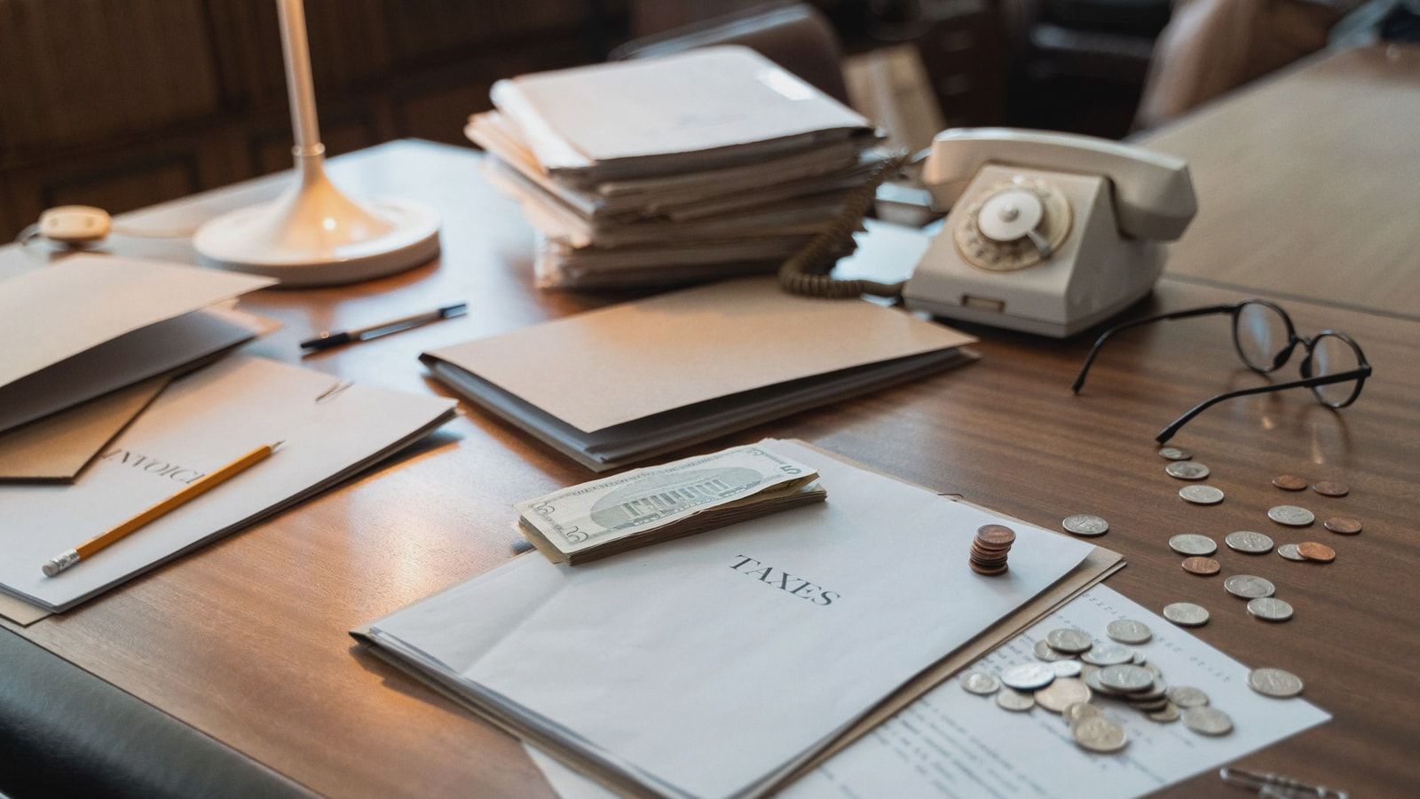 Close-up of an office desk with tax documents, coins, glasses, and an old phone, symbolizing finance and organization.