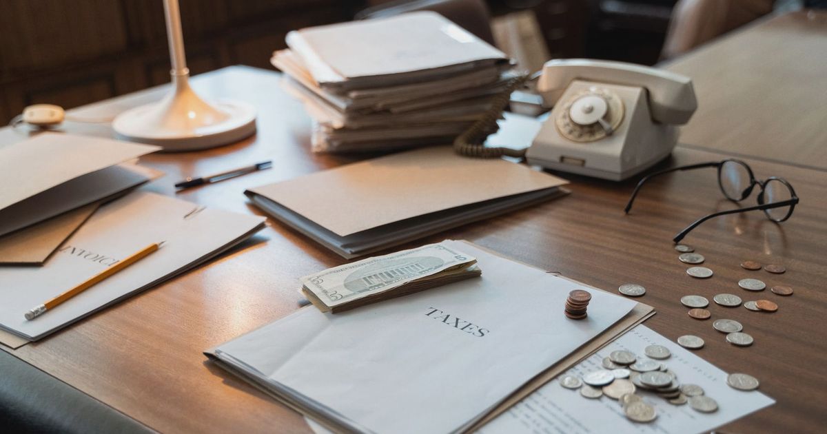 Close-up of an office desk with tax documents, coins, glasses, and an old phone, symbolizing finance and organization.