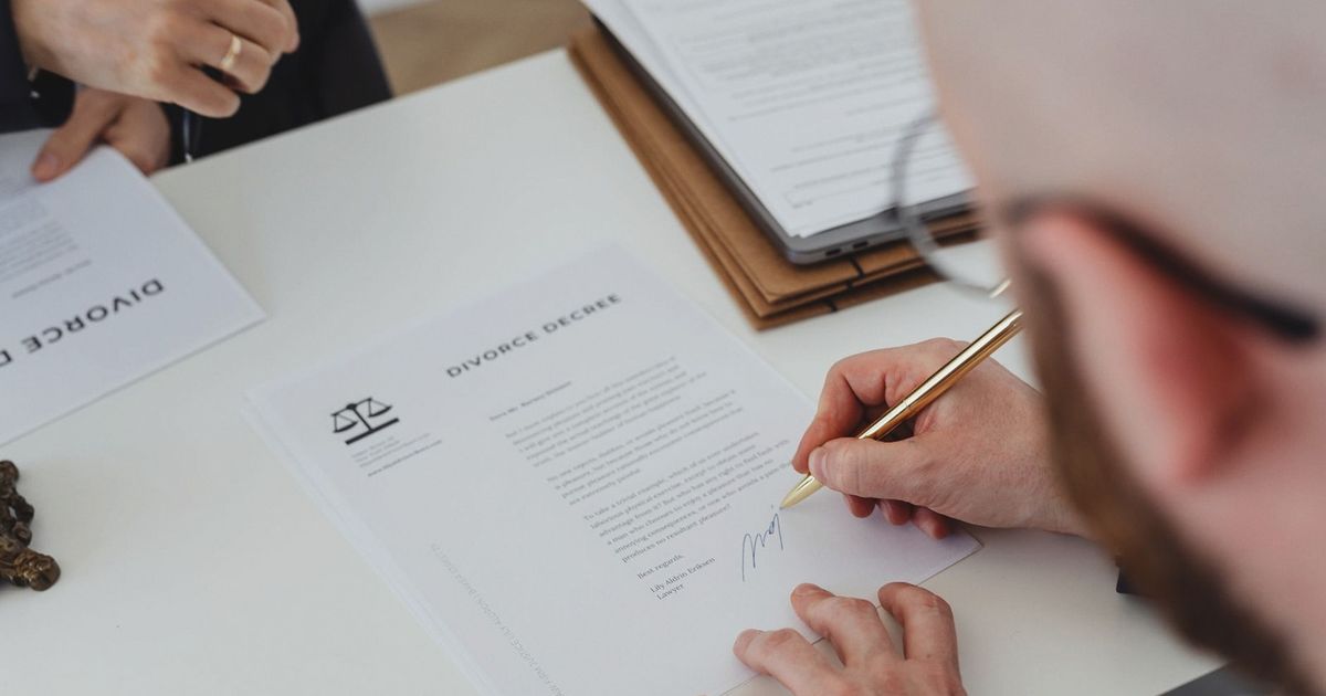 Close-up of a person signing a divorce decree on a desk.