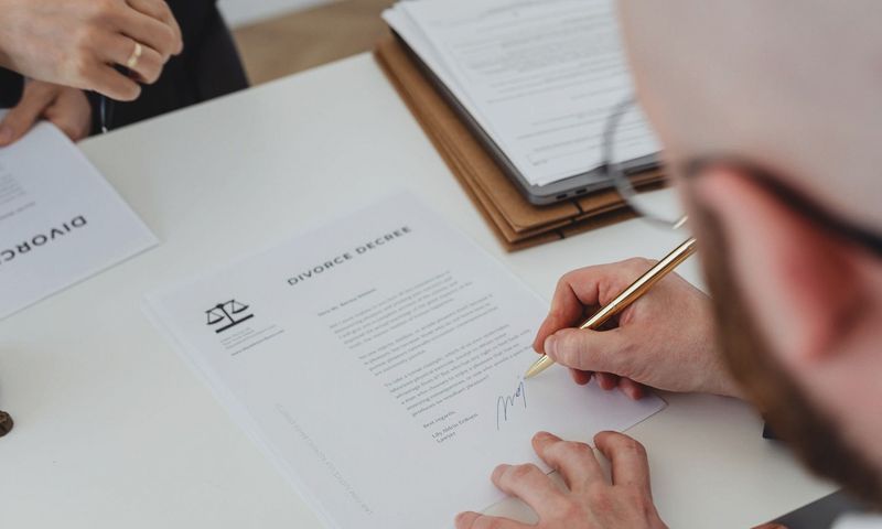 Close-up of a person signing a divorce decree on a desk.