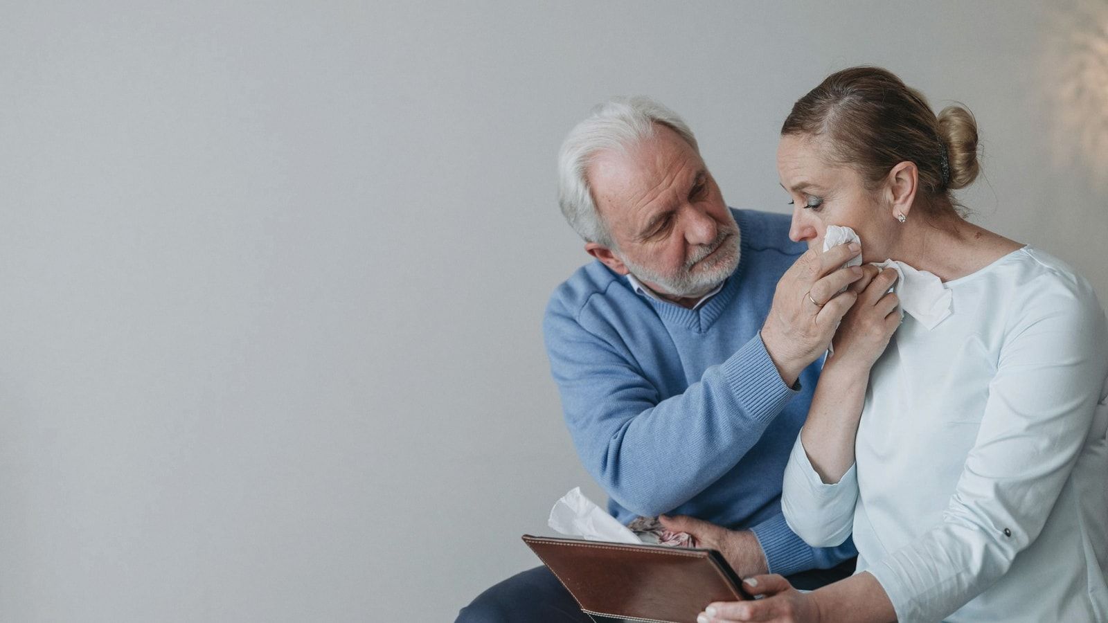 A senior couple embracing and wiping away tears while reminiscing with a photo album.