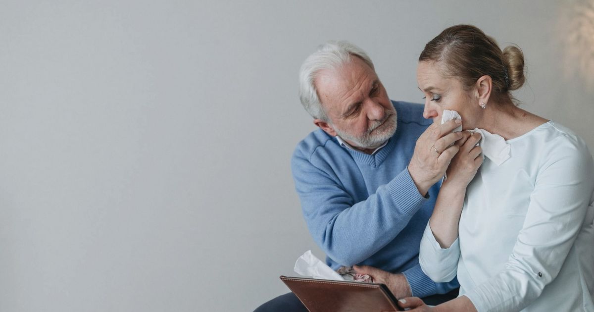 A senior couple embracing and wiping away tears while reminiscing with a photo album.
