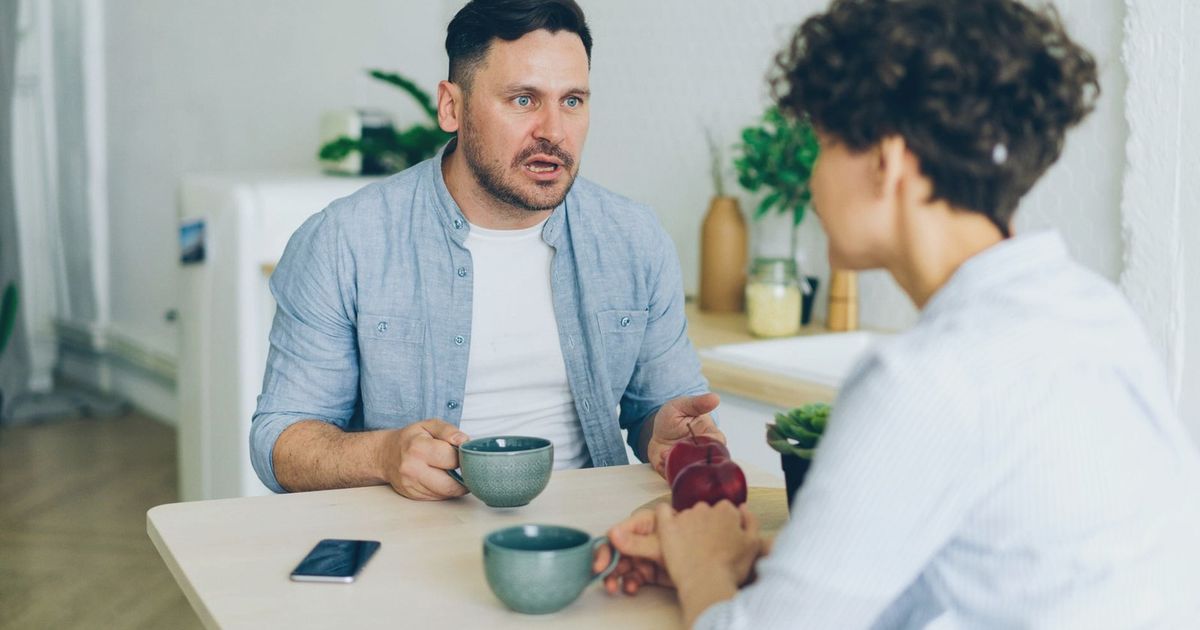 Couple having a serious conversation at the kitchen table with coffee cups.