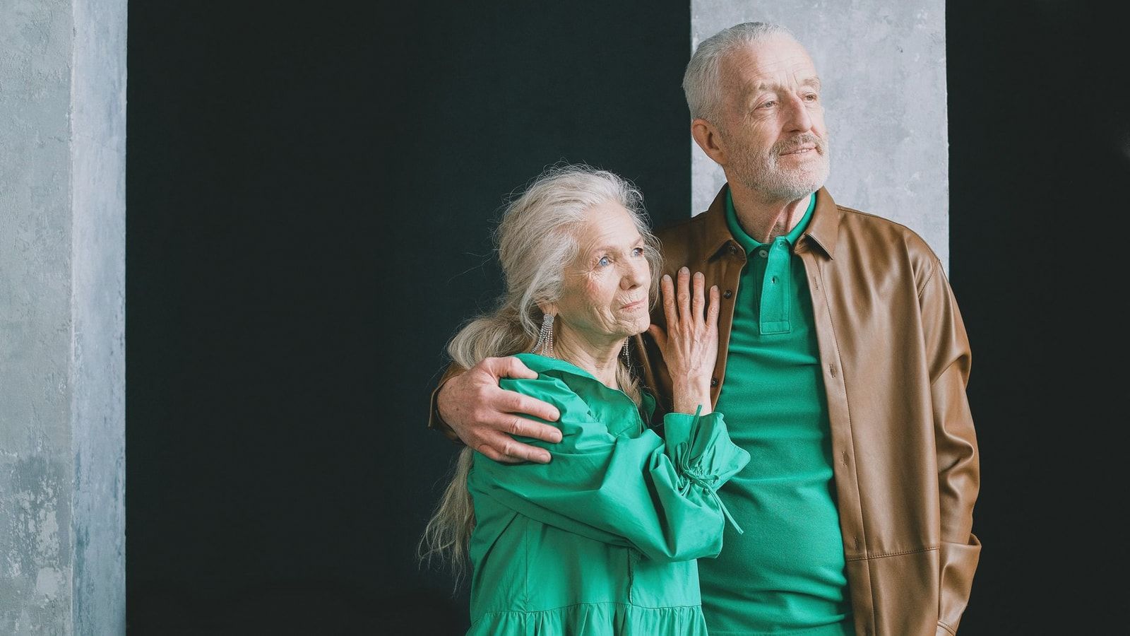 An elderly couple standing and embracing, clad in earthy tones, conveying love and togetherness.