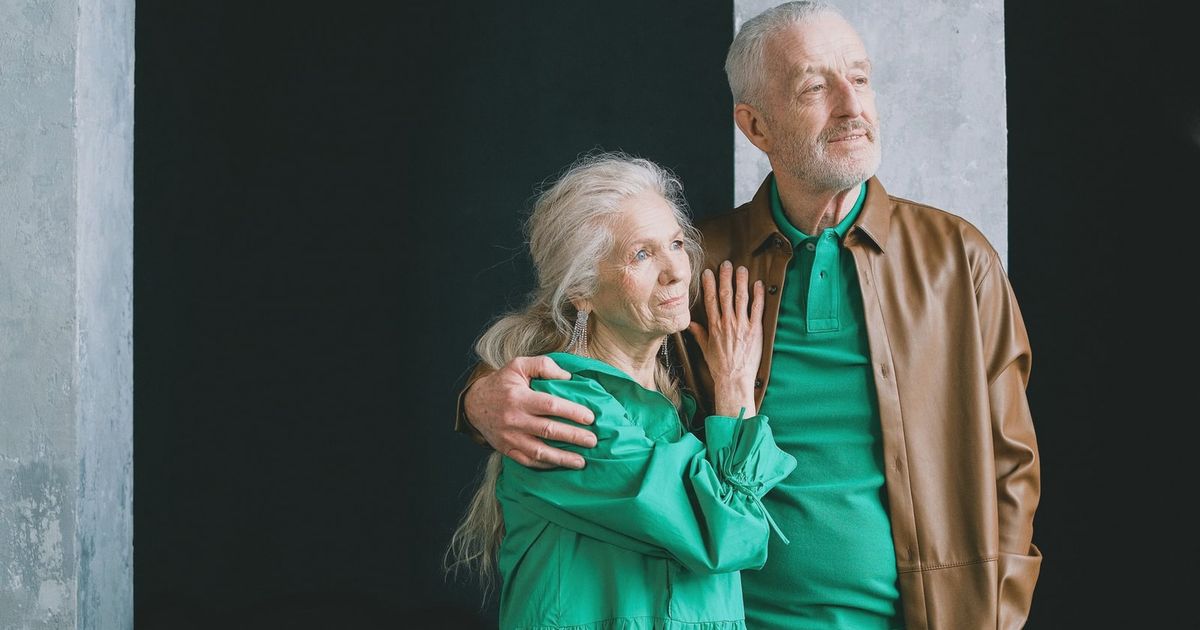 An elderly couple standing and embracing, clad in earthy tones, conveying love and togetherness.