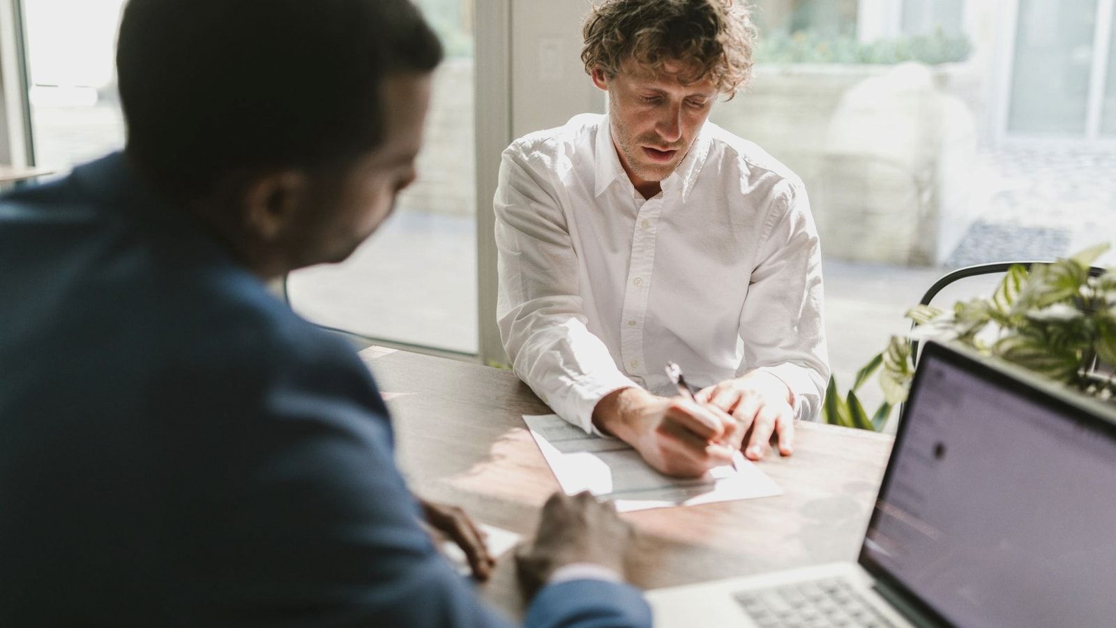 Two men collaborating in a modern office, reviewing and signing documents.