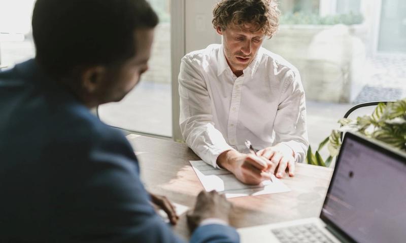 Two men collaborating in a modern office, reviewing and signing documents.