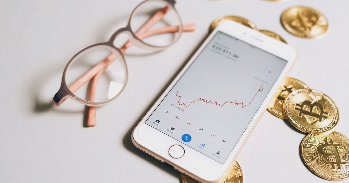 Smartphone displaying cryptocurrency graph alongside bitcoin coins and eyeglasses.