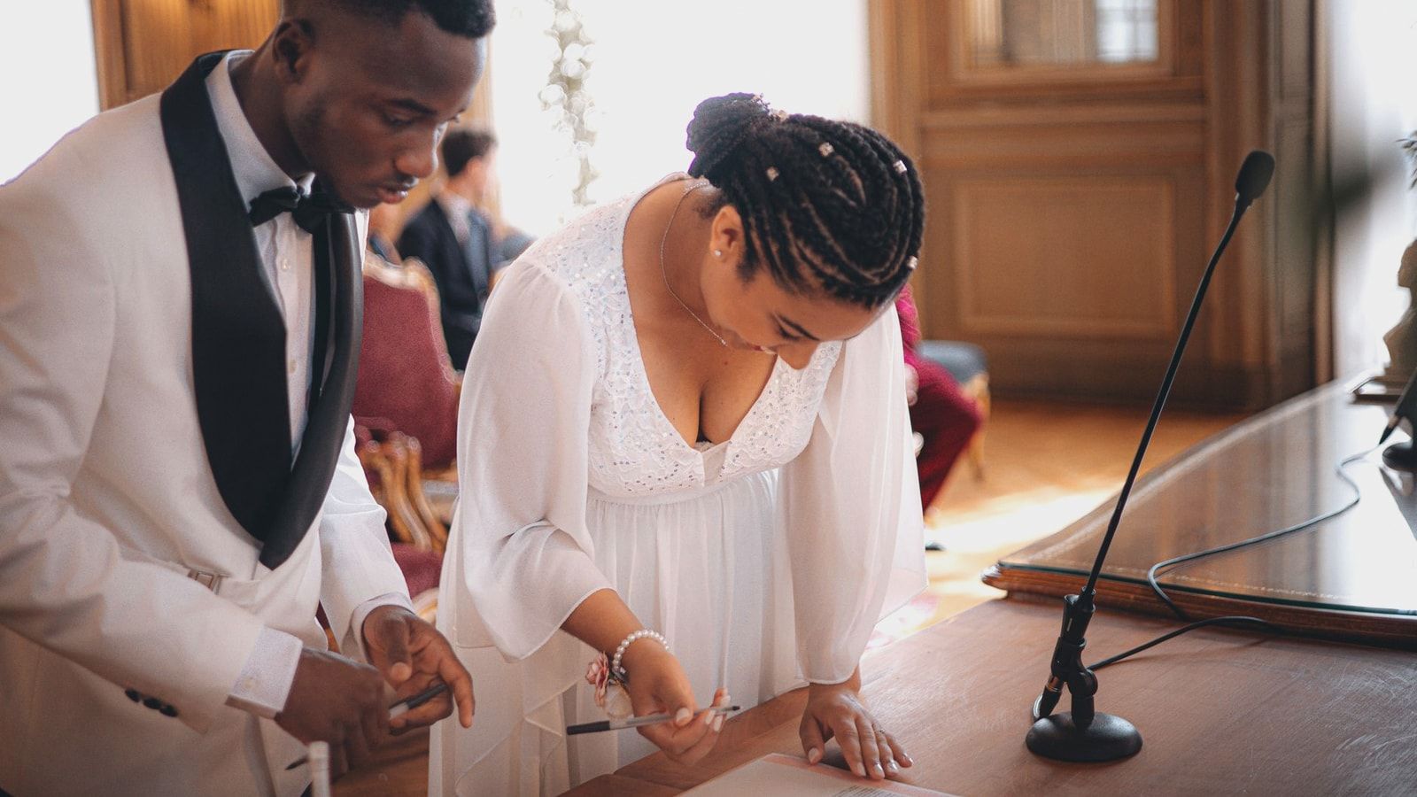 Bride and groom signing documents at a formal indoor wedding ceremony.