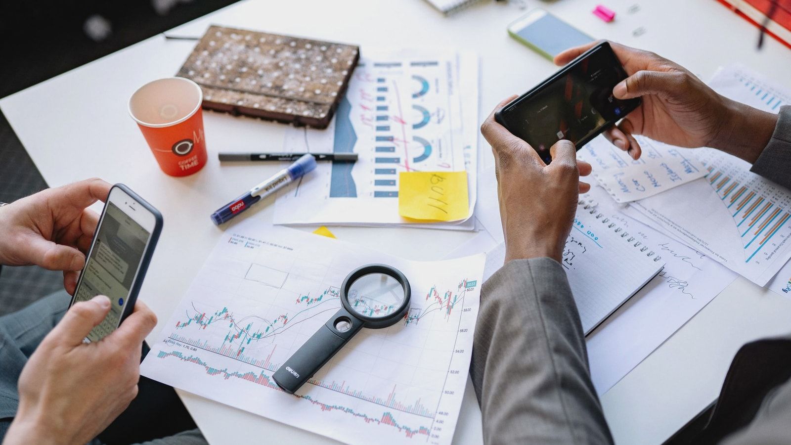 Two professionals analyzing data and graphs with smartphones on a white table.