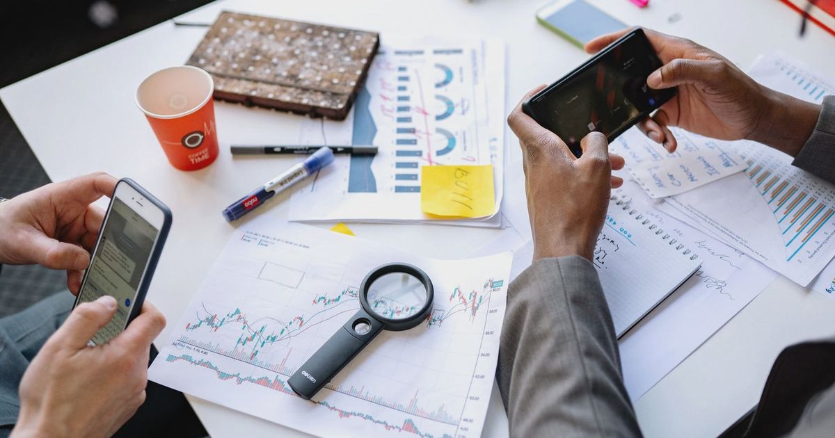 Two professionals analyzing data and graphs with smartphones on a white table.