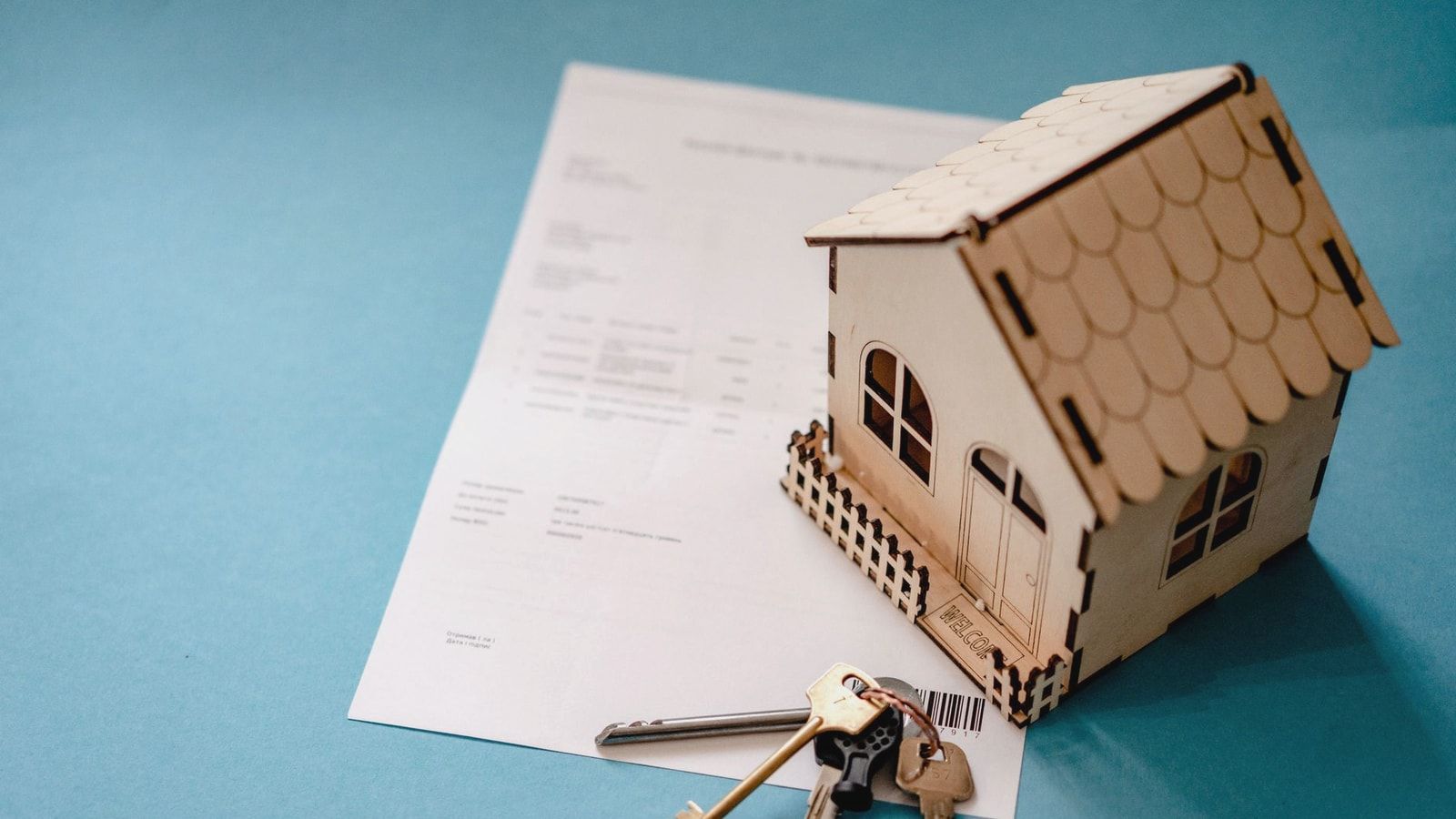 Miniature wooden house with keys and contract symbolizing real estate transactions.