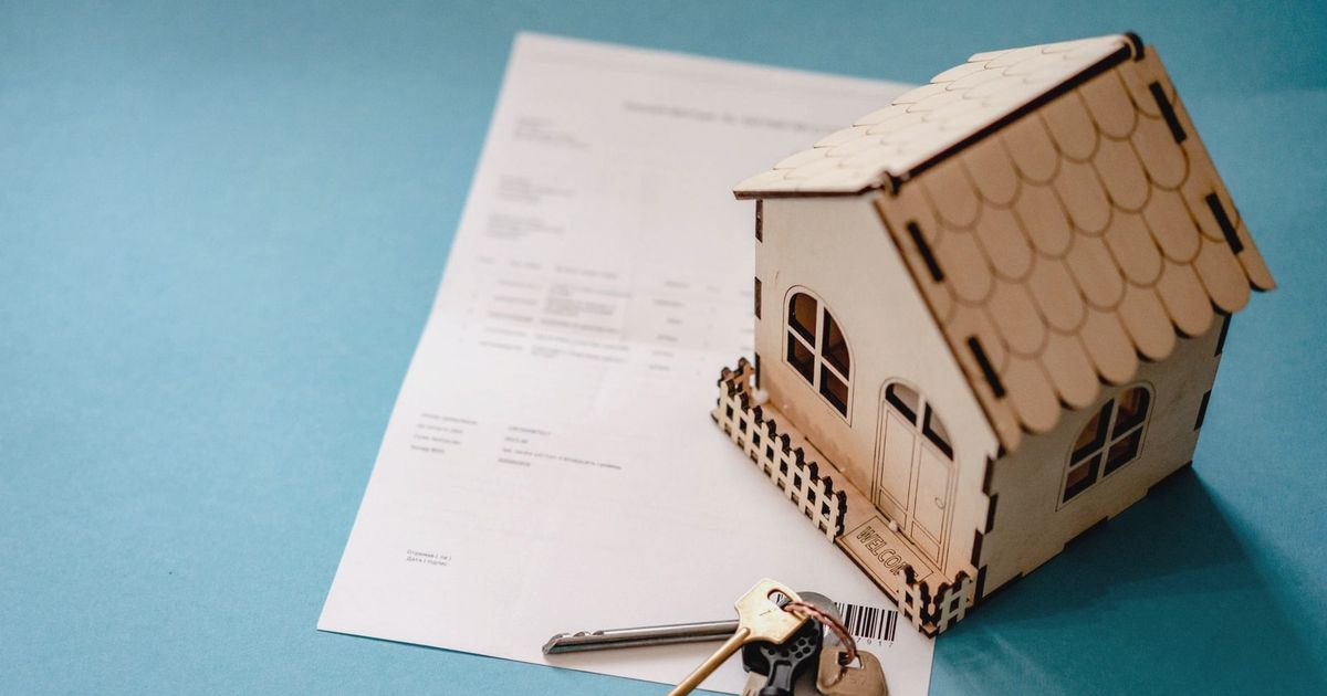 Miniature wooden house with keys and contract symbolizing real estate transactions.