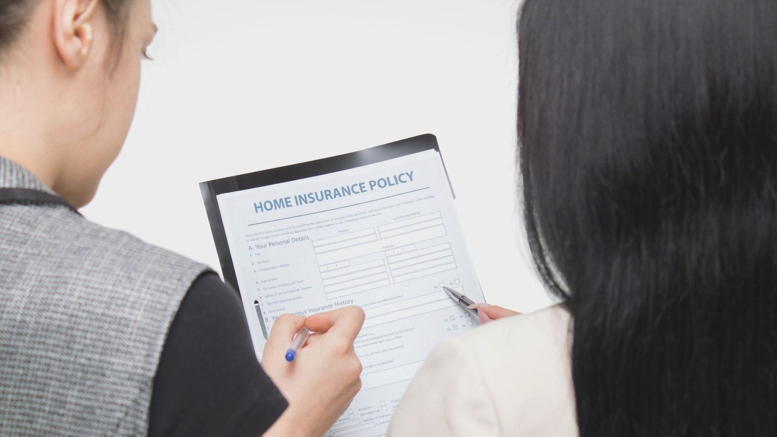 Two women examining home insurance policy form, focused on details.