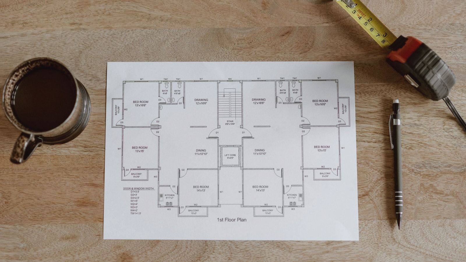 Top view of set of plan of room with tape measure and pen for work for architect with cup with coffee on wooden table in soft daylight