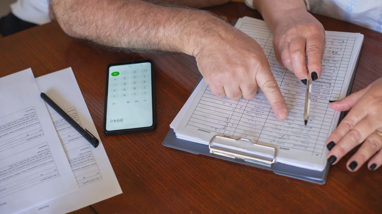 Close-up of hands working on finance planning with documents and a smartphone calculator.