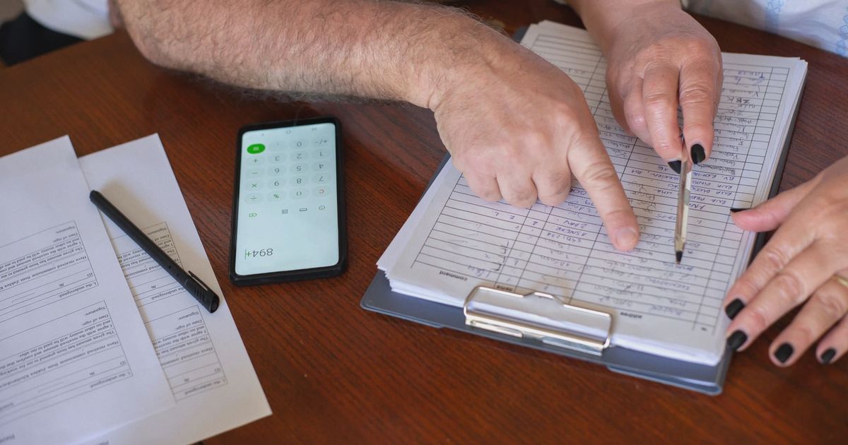 Close-up of hands working on finance planning with documents and a smartphone calculator.