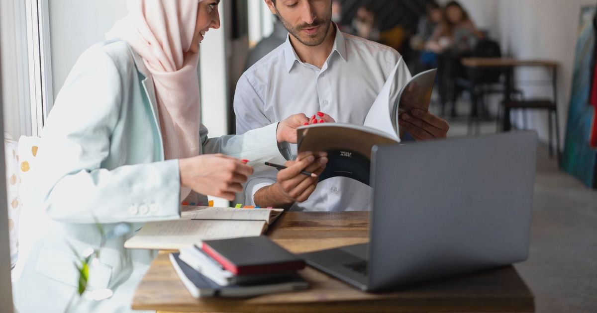 Two adults collaborating over work material in a cafe setting. Ideal for teamwork and study themes.