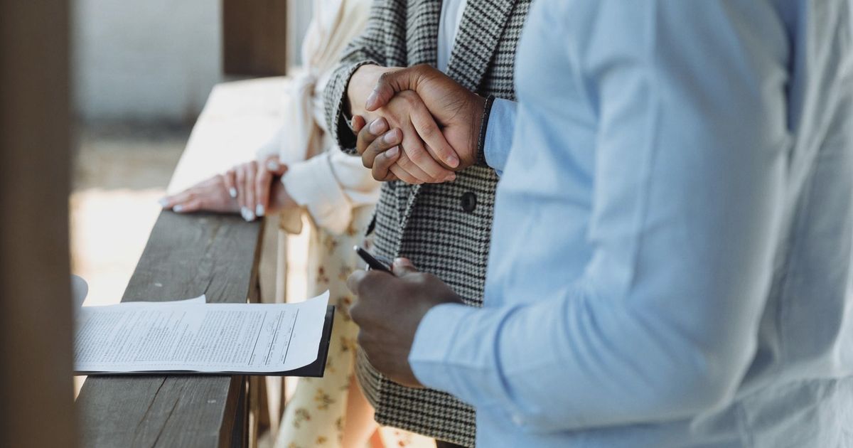 A close-up of hands shaking over a signed property agreement, symbolizing a successful real estate deal.