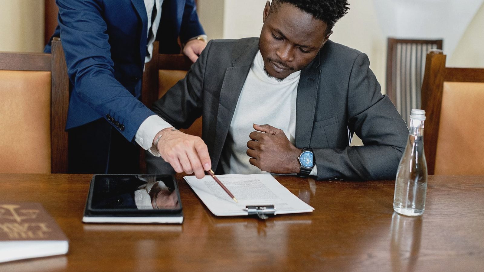 Two businessmen in a legal consultation reviewing a document with a tablet on the desk.