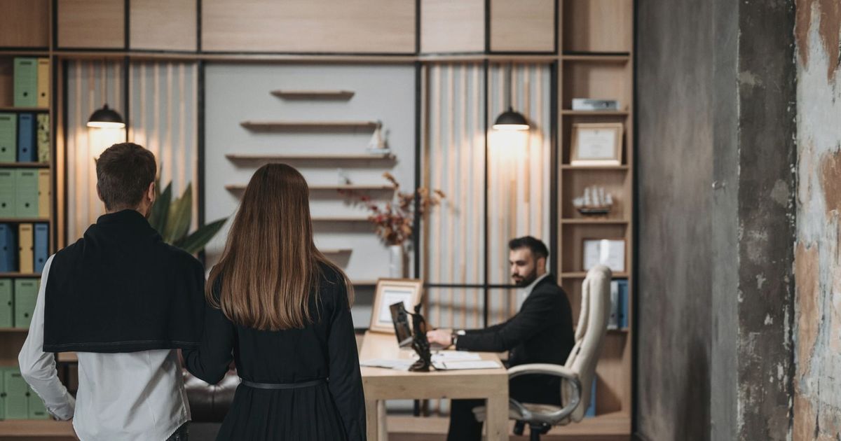 A couple approaches a lawyer in a contemporary office setting for a professional consultation.