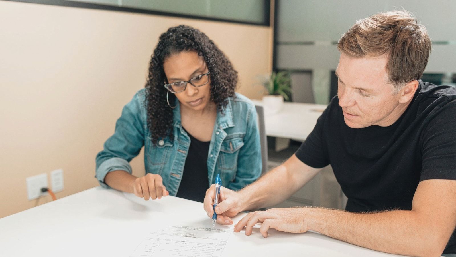 A couple working together to sign important legal documents at a desk in an office setting.