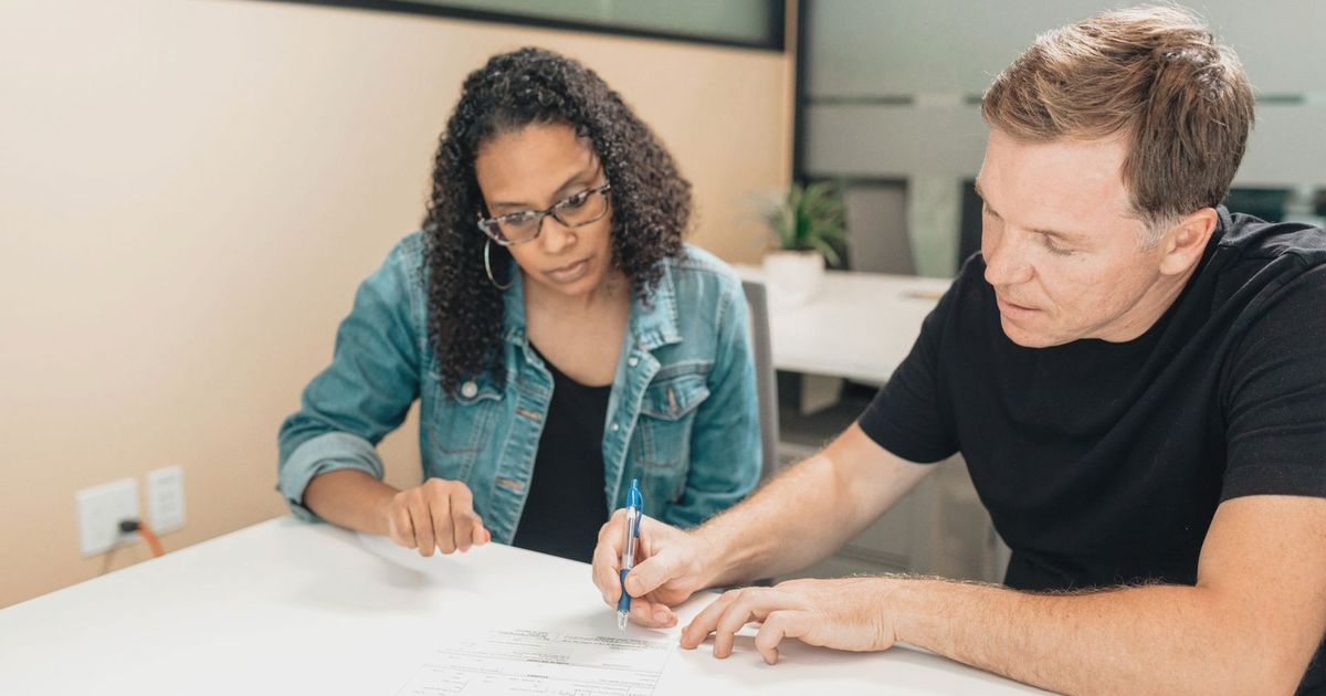 A couple working together to sign important legal documents at a desk in an office setting.