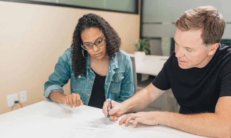 A couple working together to sign important legal documents at a desk in an office setting.