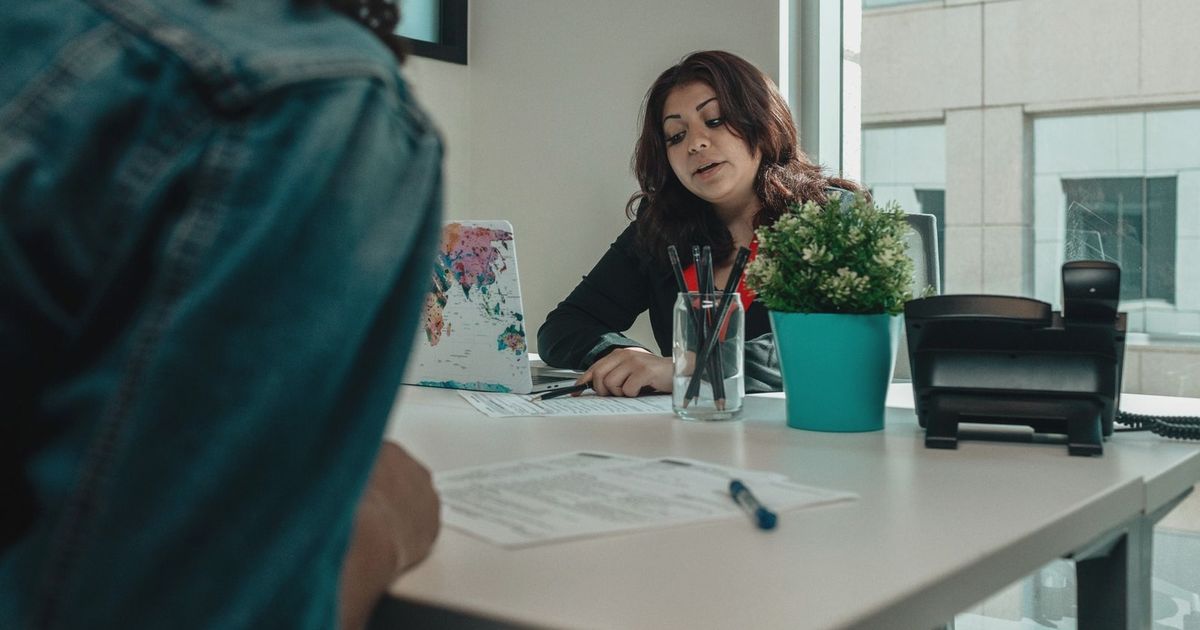 Two individuals in an office engaged in a discussion with paperwork.