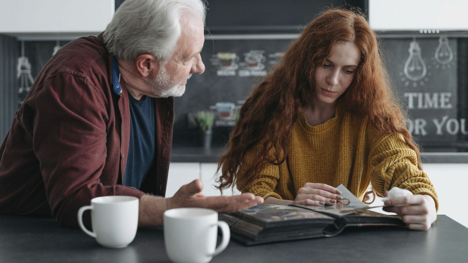 Elderly man and young woman looking at a photo album together, evoking emotions and memories.